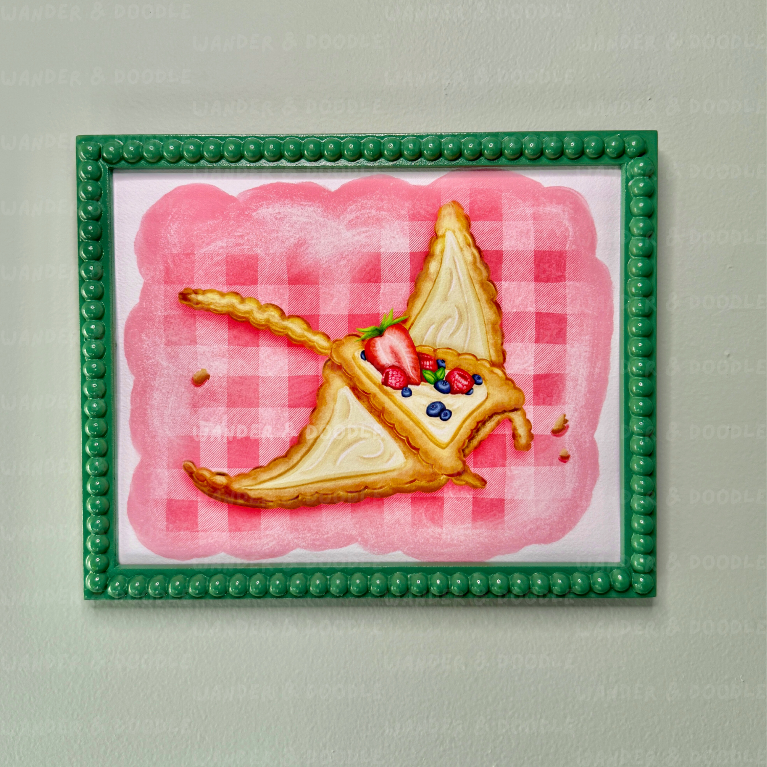 Framed artwork of a slice of pie in the shape of a manta ray with berries on a pink checkered background