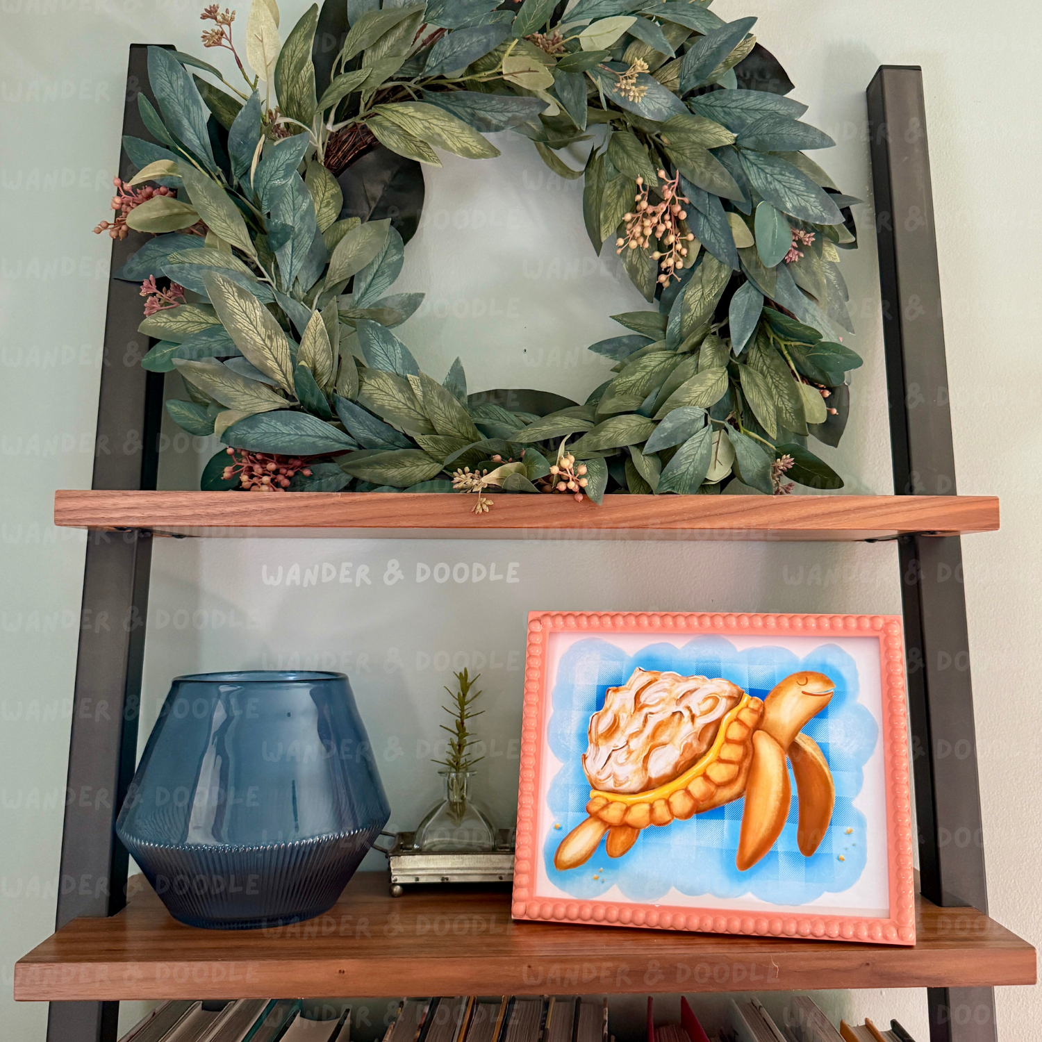 Decorative shelf with a wreath, blue vase, and framed turtle  in the shape of a lemon meringue pie artwork.